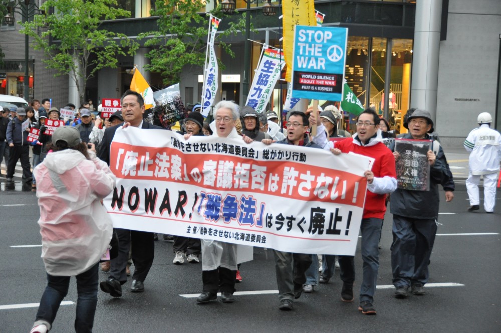 多くの通勤帰りの人が通る札幌の中心街を、デモ行進する参加者